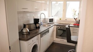 Une cuisine compacte équipée d’un lave-linge, d’un grille-pain, d’un four à micro-ondes, d’un évier et d’une cuisinière.