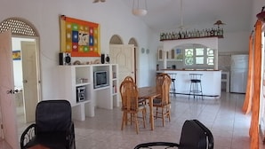 Ett rymligt vardagsrum med ett matbord, stolar, en TV och en köksdel med en bardisk.