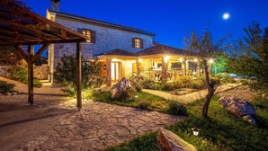 Una casa de piedra con un porche cubierto, un camino de piedra y un jardín con rocas y plantas.
