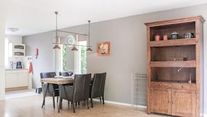 A dining area with a wooden table and chairs, a wooden cabinet with shelves, and a kitchen in the background. - Amazing home in Winterswijk with WiFi (Winterswijk)