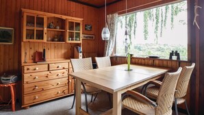 A wooden interior with a dining table, wicker chairs, a wooden cabinet with glass doors, and a window with a view of greenery. - Cozy home in Ejstrupholm with kitchen (Ejstrupholm)