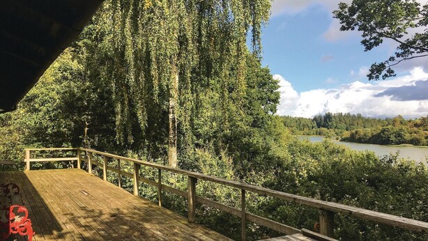 A wooden deck with a railing overlooking a river and forested area. - Cozy home in Ejstrupholm with kitchen (Ejstrupholm)