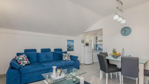 A modern living room with a blue sofa, a glass coffee table, and a dining area with a white table and chairs. - 1 bedroom awesome apartment in Stara Baska (Stara Baska)