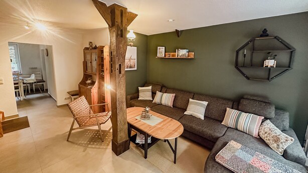 A living room with a wooden coffee table, a sofa with patterned cushions, a bookshelf, and a hexagonal wall shelf. - Groat Fleet **** - Groat Fleet (Neuenkirchen)