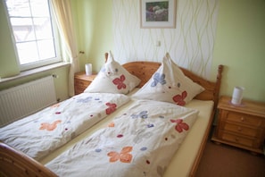 Un lit double avec une literie à motifs floraux, une tête de lit en bois, une table de chevet avec une lampe et une fenêtre avec des rideaux.