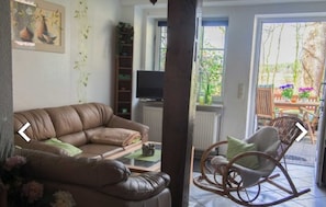 Un salon avec un canapé en cuir marron, un fauteuil à bascule en bois, une télévision et une bibliothèque.