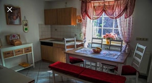 Une cuisine avec des meubles en bois, une table à manger avec des coussins rouges et une fenêtre ornée de rideaux à motifs floraux.