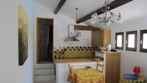 A compact kitchen with a dining area, featuring a tiled backsplash, wooden cabinets, and a chandelier.