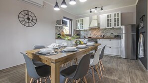 Een moderne keuken met witte kasten, een roestvrijstalen koelkast en een eethoek met een houten tafel en stoelen.