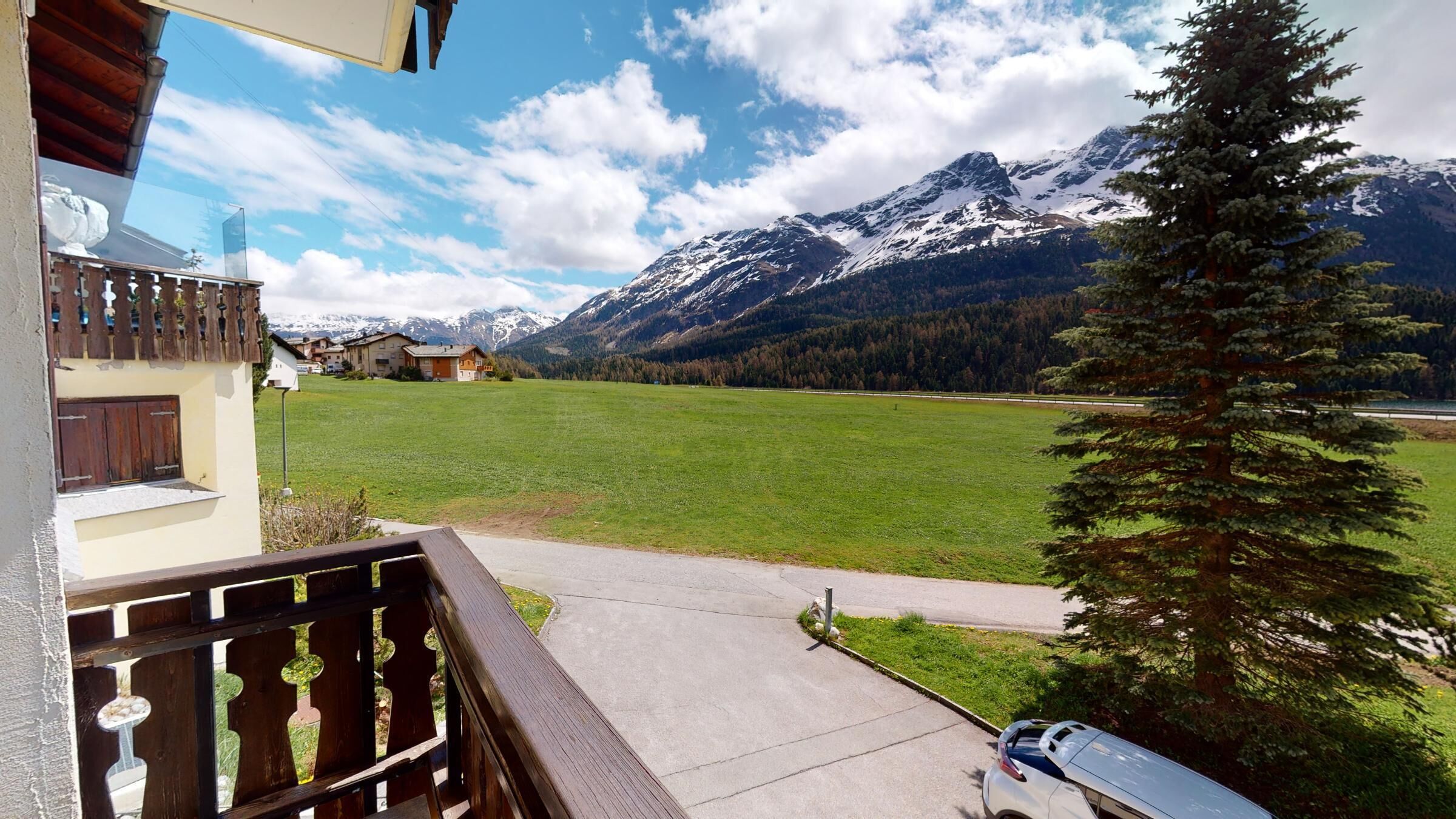 Un balcon donnant sur un champ verdoyant et des montagnes aux sommets enneigés.