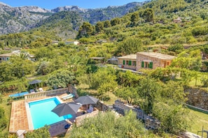 Une piscine dotée d’une terrasse en pierre, entourée de verdure et avec une chaîne de montagnes en toile de fond.