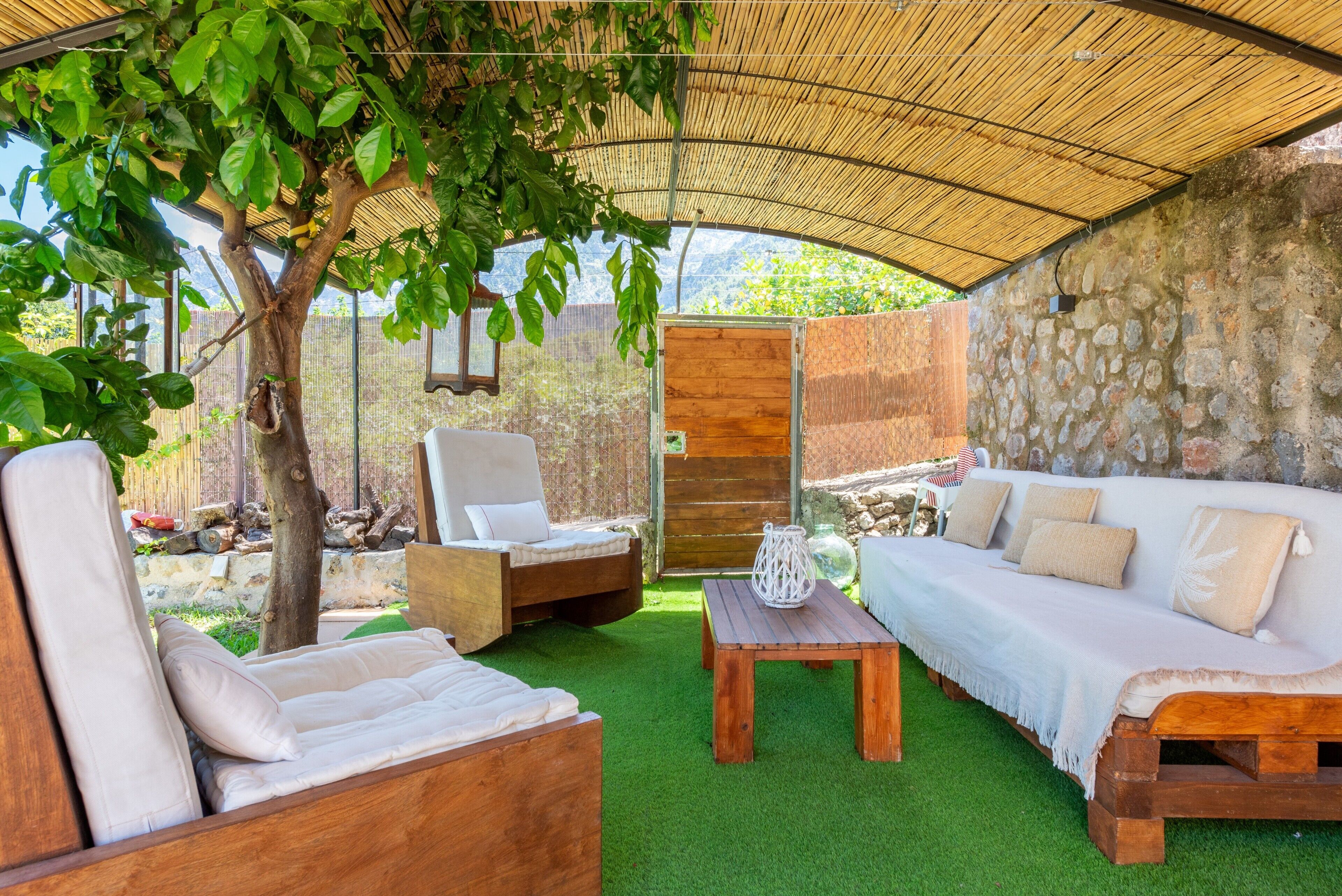 A covered outdoor seating area with a wooden bench, a cushioned sofa, and a lounge chair.