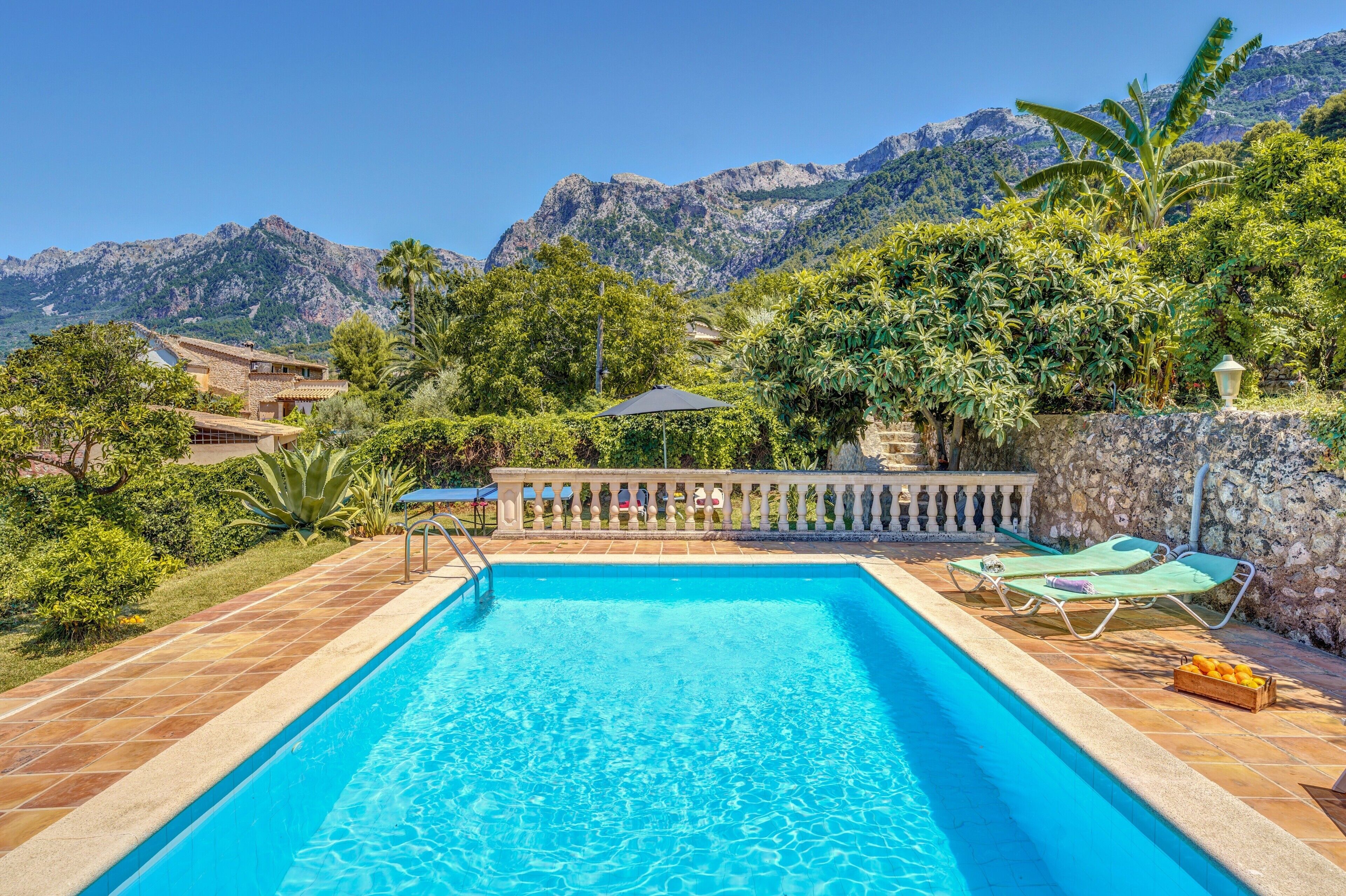 A swimming pool with a stone border, lounge chairs, and a view of mountains.