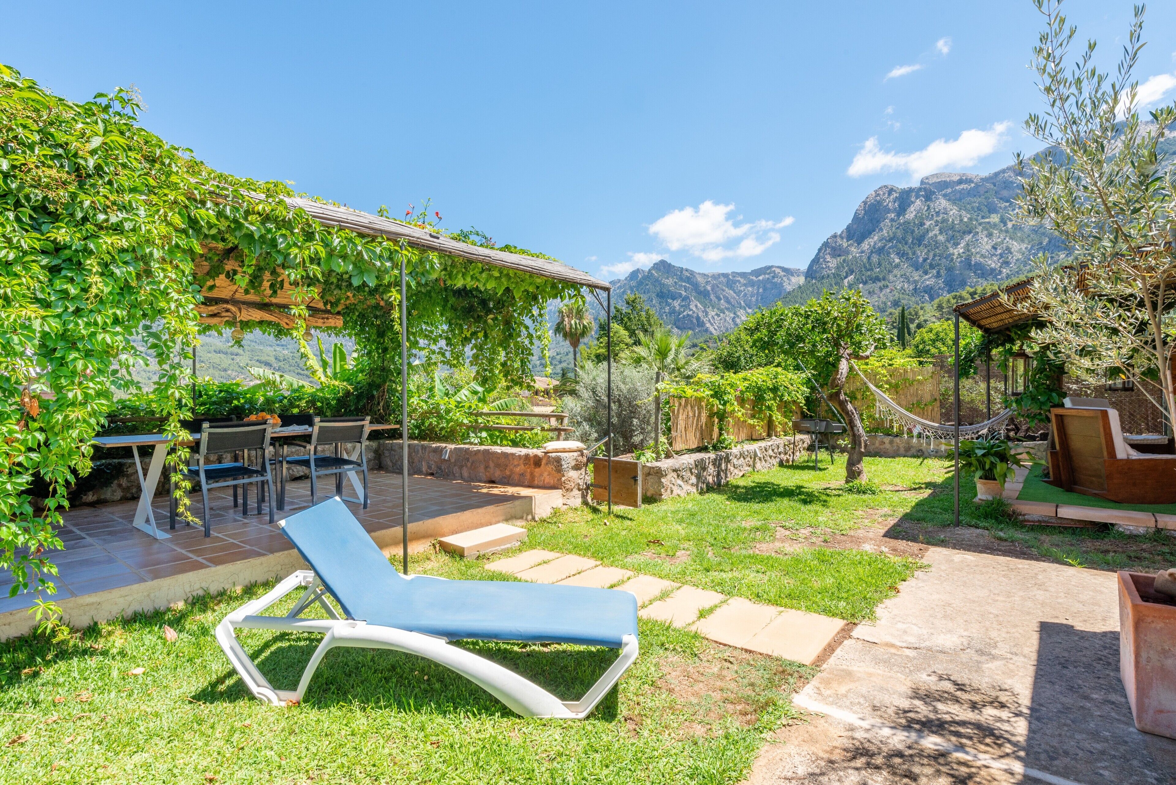 A garden with a lounge chair, outdoor furniture, and a pergola covered with greenery.