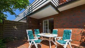 Une terrasse avec une table blanche et quatre chaises, un mur en briques et une clôture en bois.