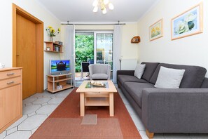 Un salon moderne avec un canapé gris, une table basse en bois et un téléviseur posé sur un meuble. On y trouve également une bibliothèque remplie de livres et un vase de fleurs.