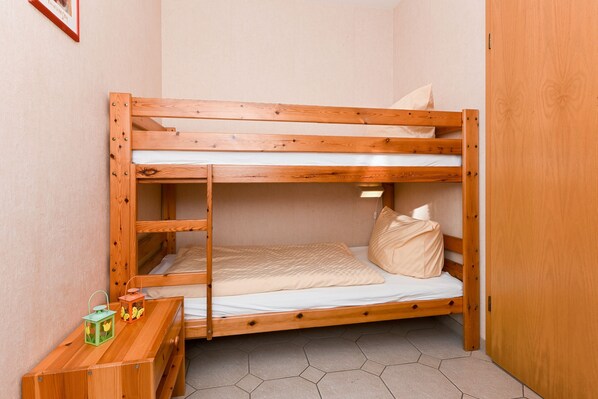 A bunk bed with a wooden frame, a small bedside table with two lanterns, and a hexagonal tiled floor. - Balthasar of Esens - house pirate island (Esens)