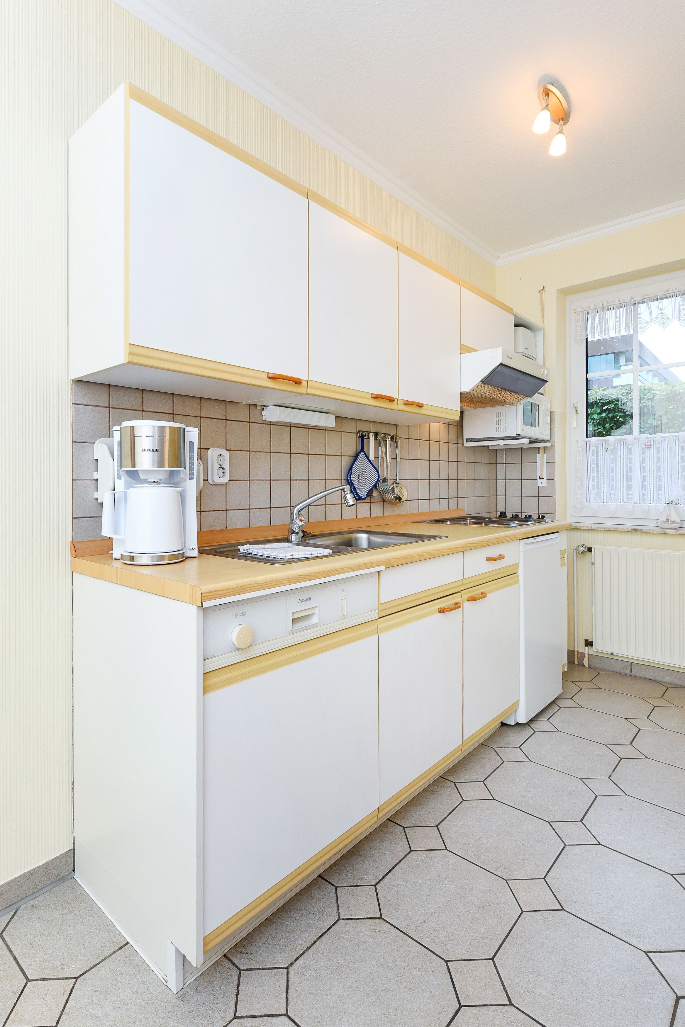 Een moderne keuken met witte kasten, een koffiezetapparaat van roestvrij staal, een spoelbak en een raam met uitzicht op groen.