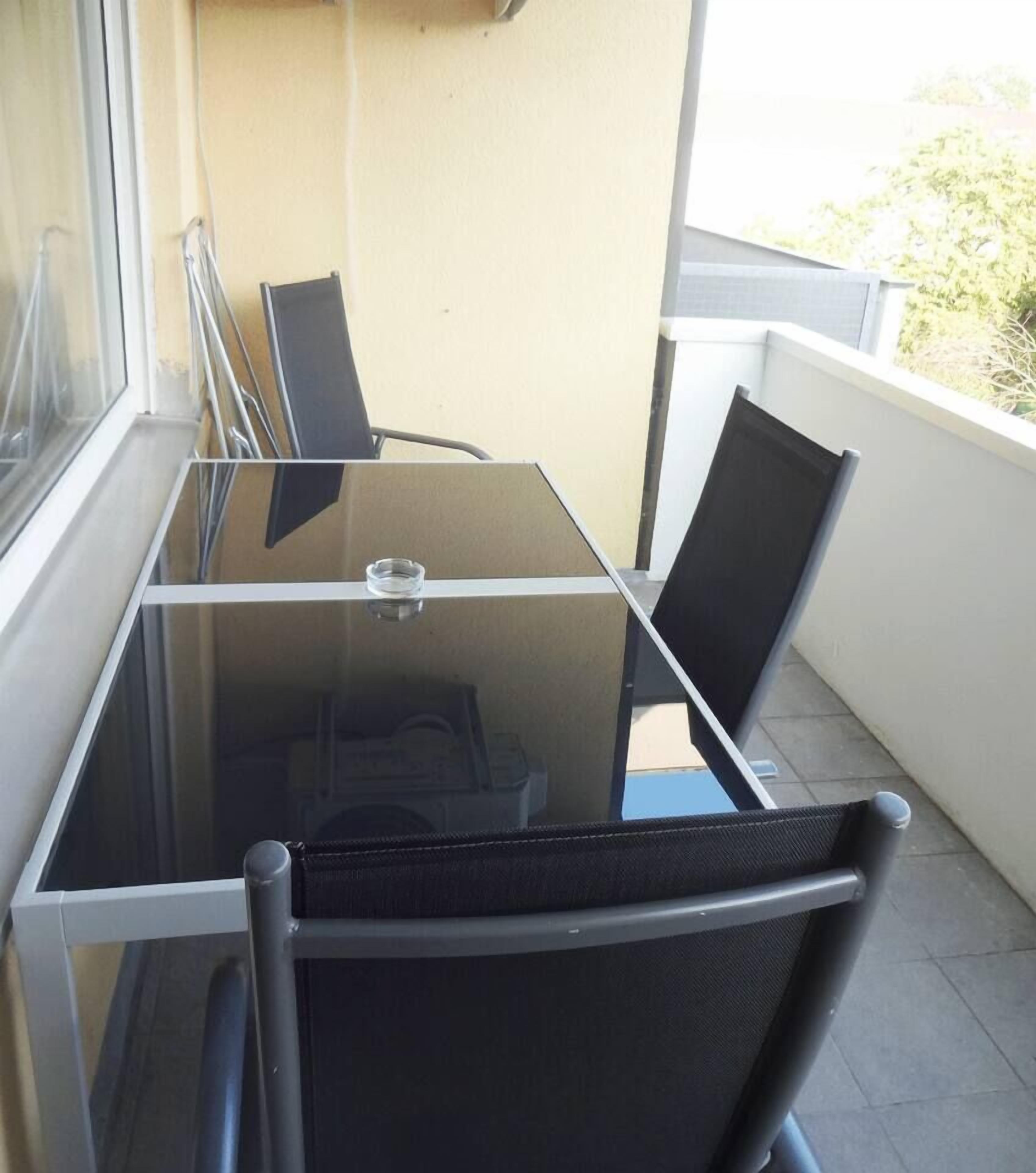 Et bord med glasplade og to sorte stole på en balkon.