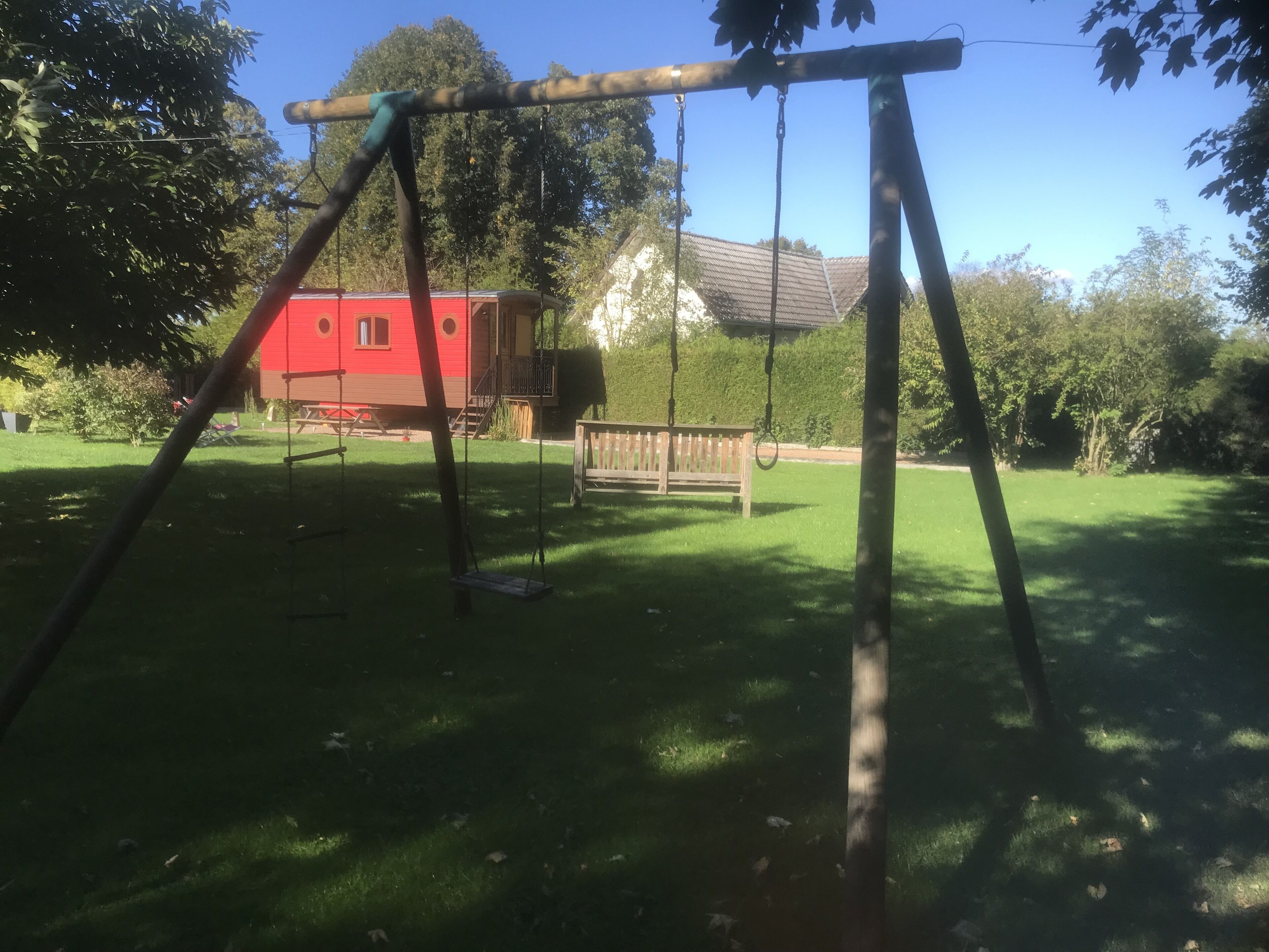 A swing set in a backyard with a red house and a wooden bench in the background.