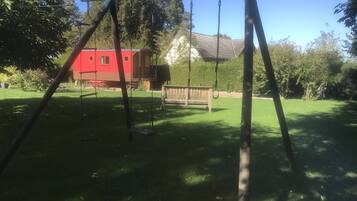 A swing set in a backyard with a red house and a wooden bench in the background.