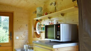 A wooden cabin kitchen with a microwave, sink, and shelves above the counter. - Unusual gite equipped to receive up to 5 people (Seux)