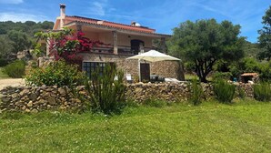 Una casa de piedra con techo de tejas rojas, un balcón con sombrilla blanca y un muro de piedra en primer plano.