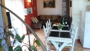 A cozy living room with a red wall, a sofa, a dining table with chairs, and a kitchen area with a refrigerator. - Charming house in central Algarve in quiet highland, only 18 km to airport (Algarve)