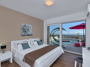 A modern hotel room with a large bed, a painting on the wall, and a view of a pool and outdoor area.