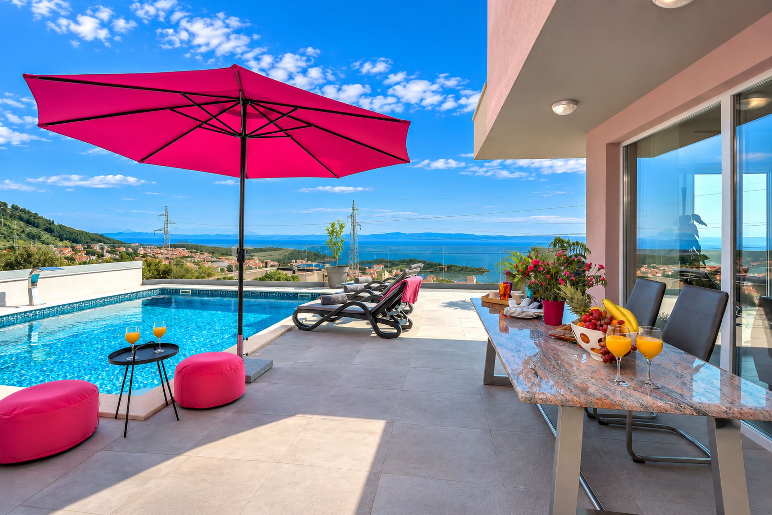 A poolside area with a red umbrella, lounge chairs, and a dining table with fruit and drinks.
