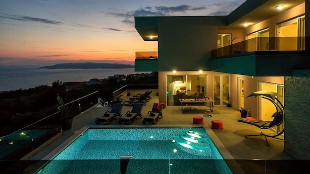 A modern house with a swimming pool, lounge chairs, and a view of the sea at dusk. - Top Features! Holiday house with heated pool with sea view, for 10 people (Makarska)