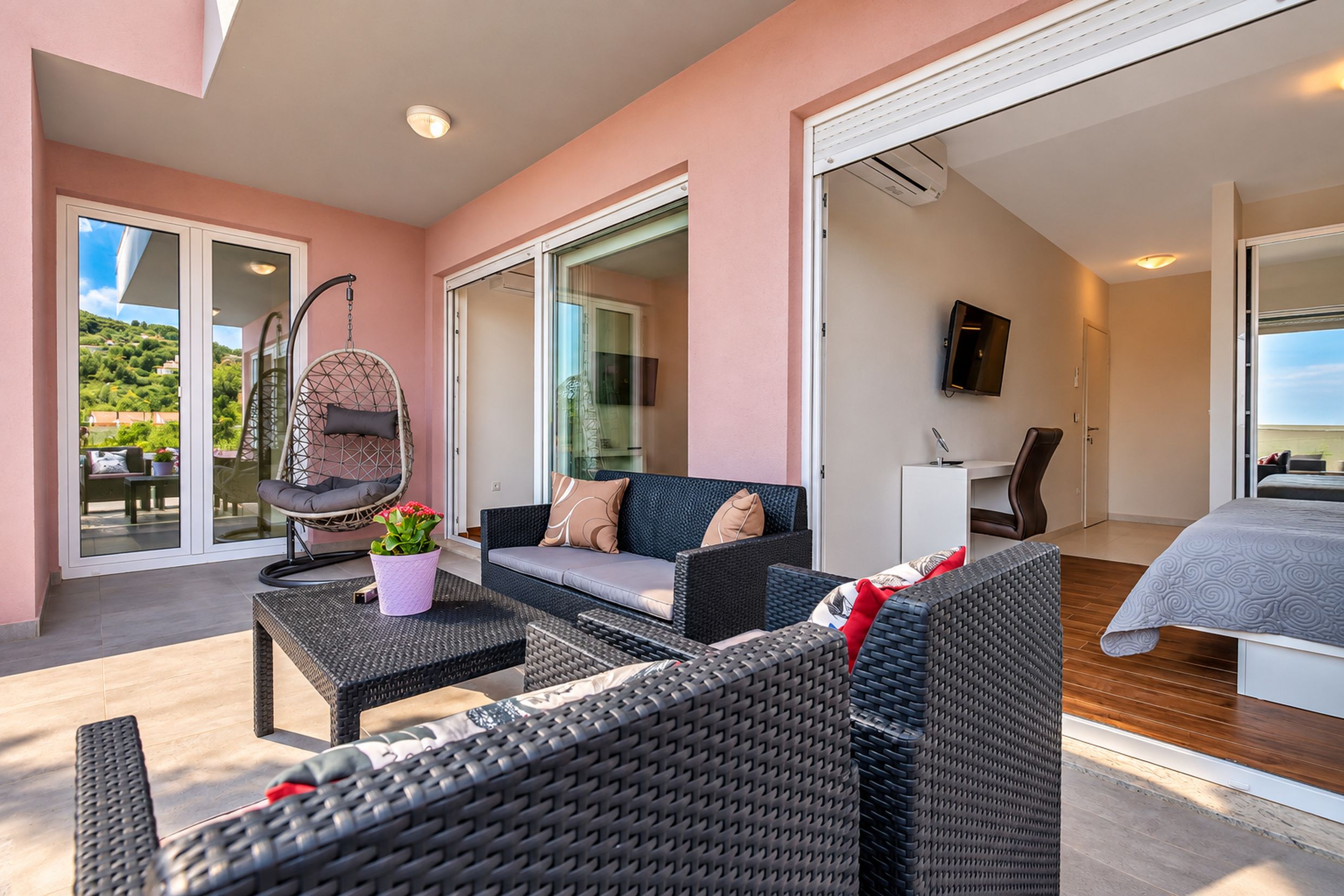 A modern interior with wicker furniture, a hanging chair, and a sofa with cushions.