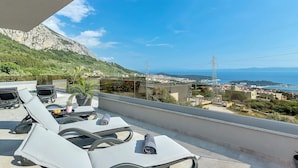 A balcony with lounge chairs and a table, overlooking a coastal town and mountains. - Top Features! Holiday house with heated pool with sea view, for 10 people (Makarska)