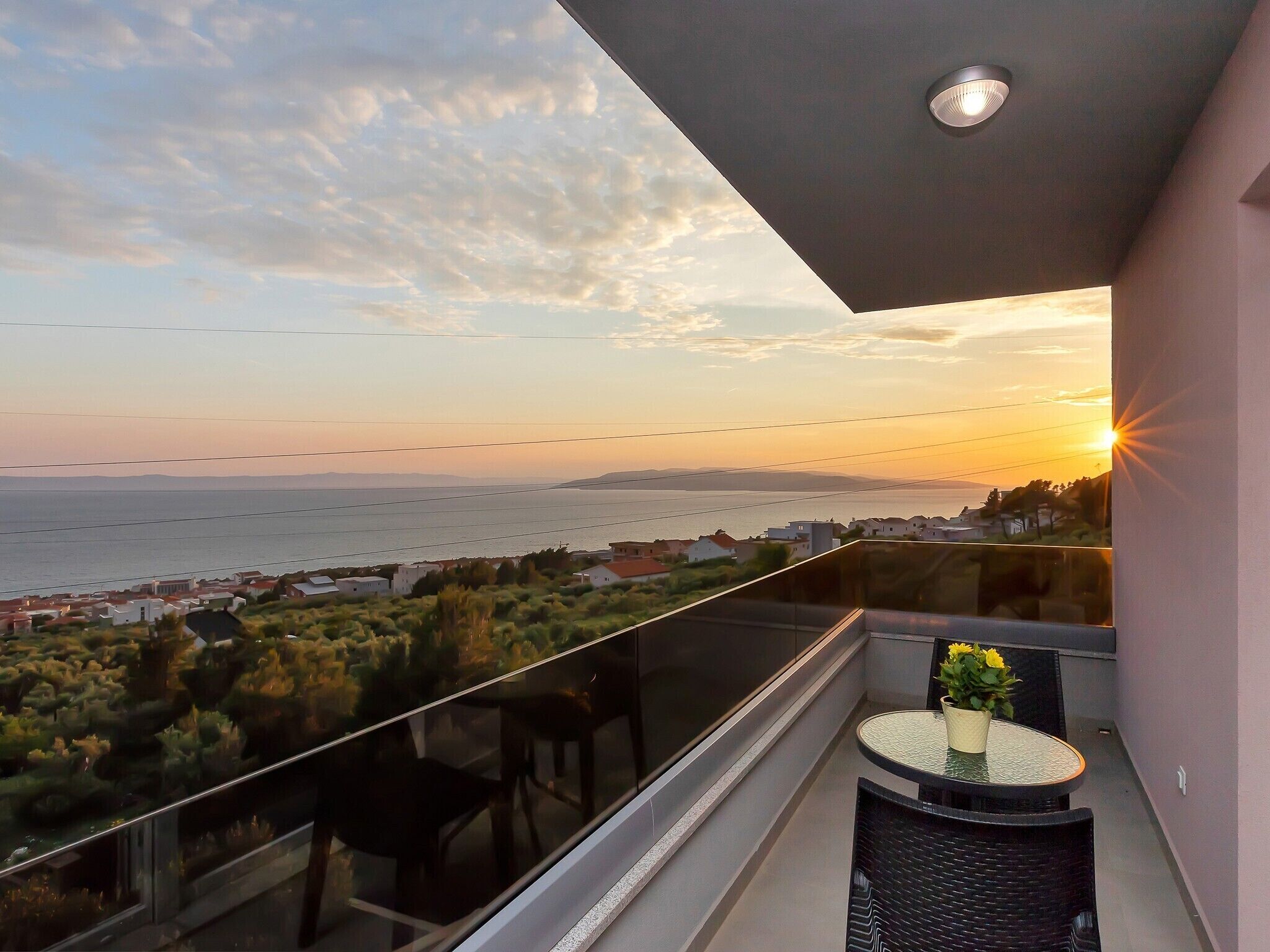 Un balcon doté d'une balustrade en verre, offrant une vue sur la côte au coucher du soleil.