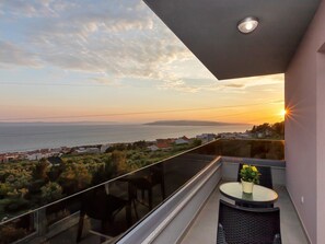 Ein Balkon mit Glasgeländer und Blick auf die Küste bei Sonnenuntergang.