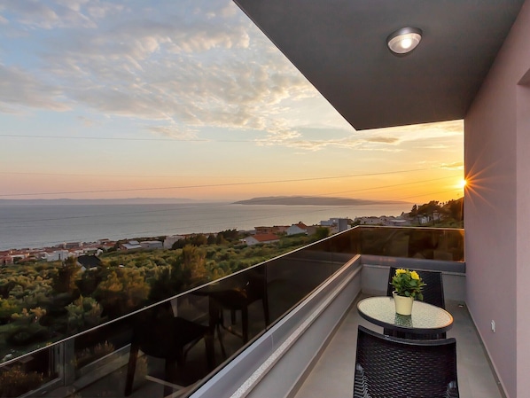 A balcony with a glass railing overlooking a coastal view during sunset.