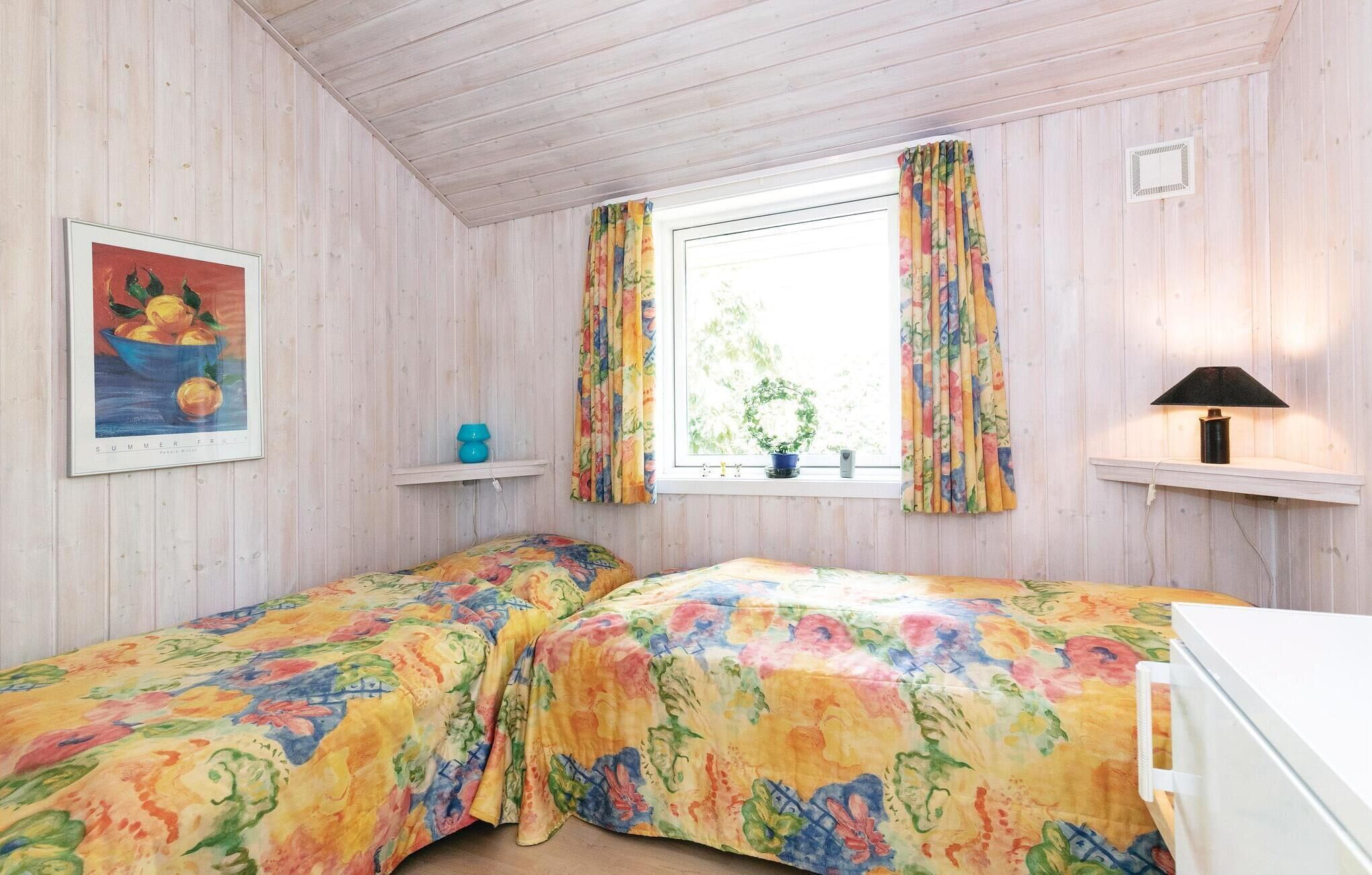 Een kamer met twee bedden, een raam met gordijnen, een lijst met een schilderij, een lamp en een plankje met een plant.