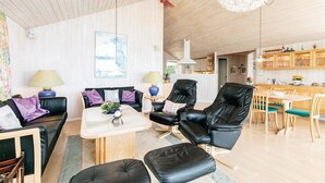 A modern living room with a sofa, two armchairs, a coffee table, and a dining area with wooden furniture. - 4 bedroom awesome home in Rønne (Rønne)