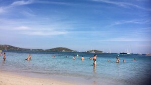 A beach with clear blue water and boats in the distance.