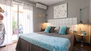 A bedroom with a large bed, a nightstand, a lamp, and a wall-mounted air conditioner.