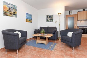 Ein Wohnzimmer mit einer Couch, zwei Sesseln, einem Couchtisch und Kunstwerken an den Wänden.