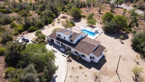 A two-story house with a swimming pool, surrounded by trees and dry grass.