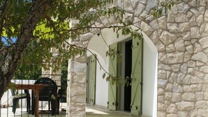 A stone building with an arched doorway, a stone wall, and a tree in the foreground.