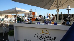 A bar area with a sign reading "Venezia GOLD" and a view of the marina with boats in the background.