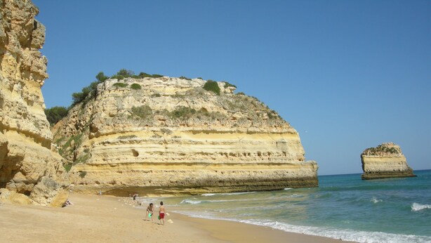 A beach with layered rock formations and clear blue water.
