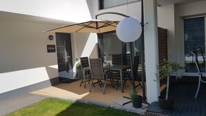 Um pátio externo com mesa e cadeiras, um lanterna de papel pendurada e plantas em vasos.