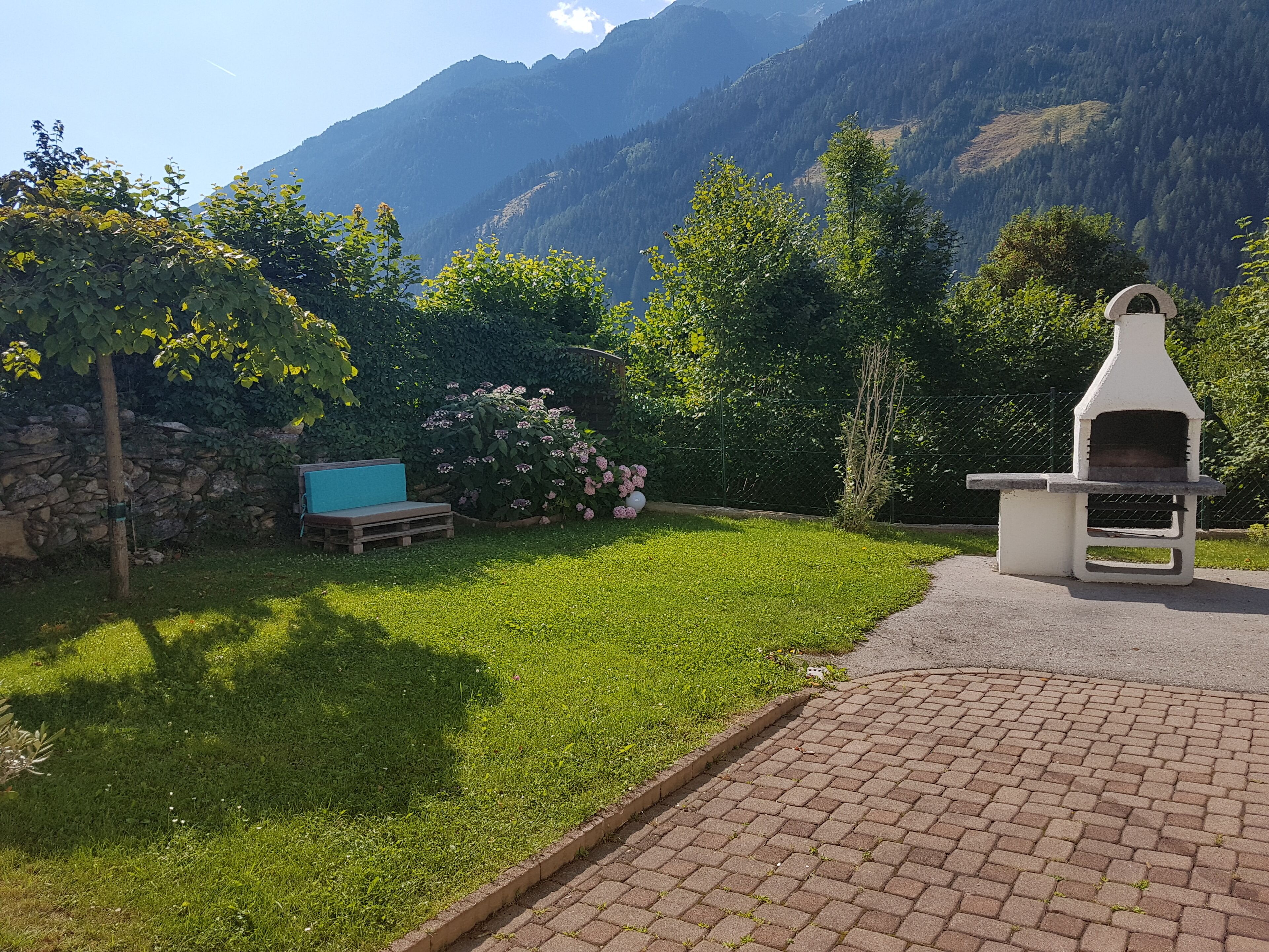 Une terrasse avec un barbecue en pierre, un coin salon extérieur bleu et un mur en pierre.