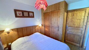 A bedroom with a bed, wooden wardrobe, and a wall-mounted lamp. - Cozy apartment at the foot of the slopes, pets allowed (Les Menuires)