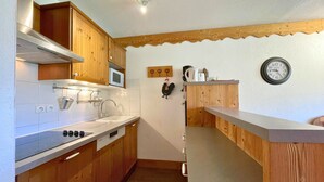 A compact kitchen with wooden cabinets, a microwave, a sink, and a clock on the wall. - Cozy apartment at the foot of the slopes, pets allowed (Les Menuires)