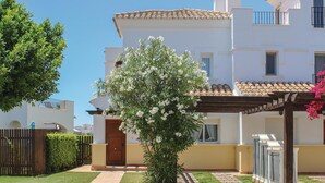 Un edificio bianco con tetto in tegole, una porta in legno e un piccolo giardino con un albero in fiore.